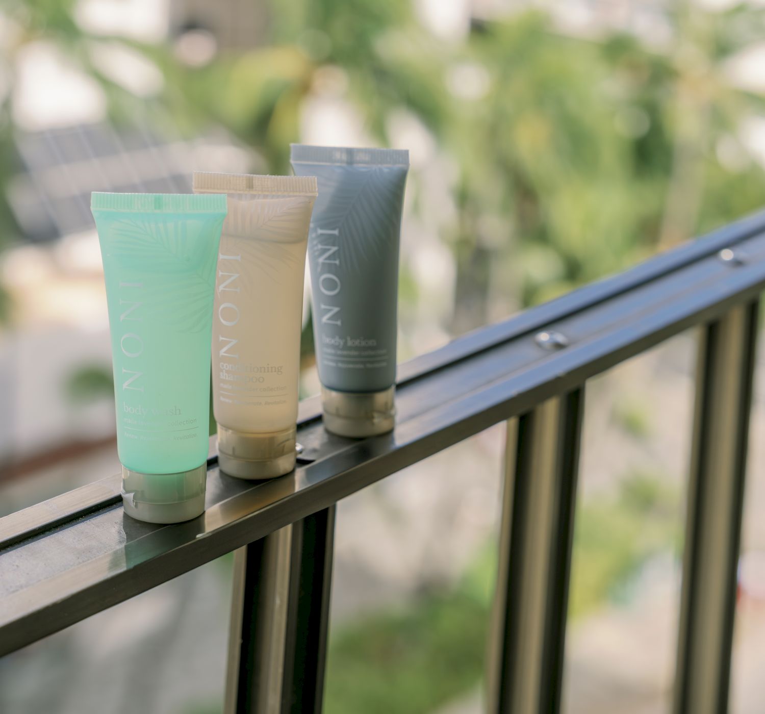 Three tubes of INONI brand products are placed on a balcony railing with a blurred background of trees.