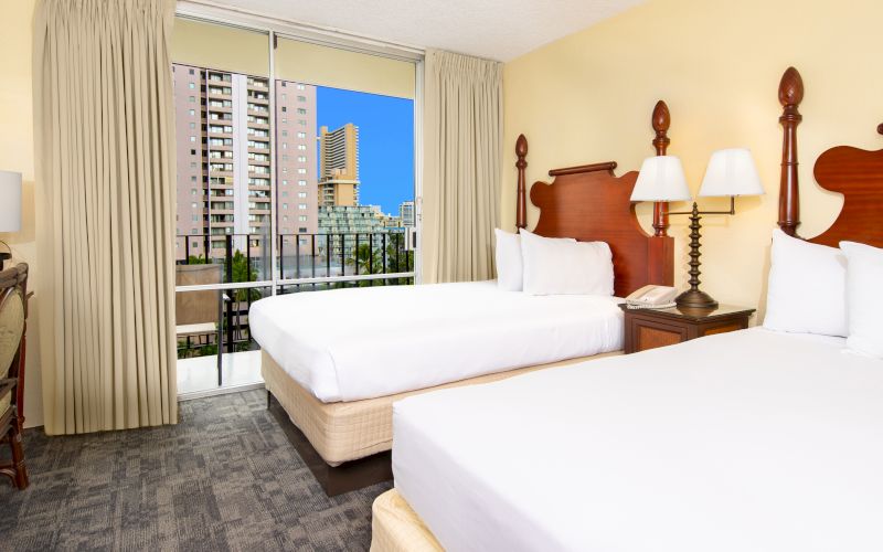 A hotel room with two beds, a balcony, and a city view.