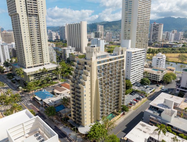 The image shows a cityscape with tall buildings, a central skyscraper, surrounding structures, and a mountainous background under a blue sky.