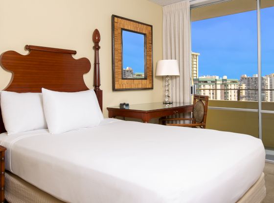 A hotel room with a large bed, desk, and window showing a city view.