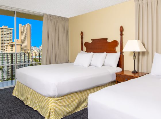 A hotel room with two beds, a balcony, and a city view.