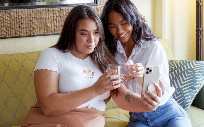 Two women sitting on a yellow couch with blue and white pillows, looking at a phone.