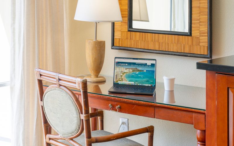 A hotel room desk with a laptop, chair, and lamp.