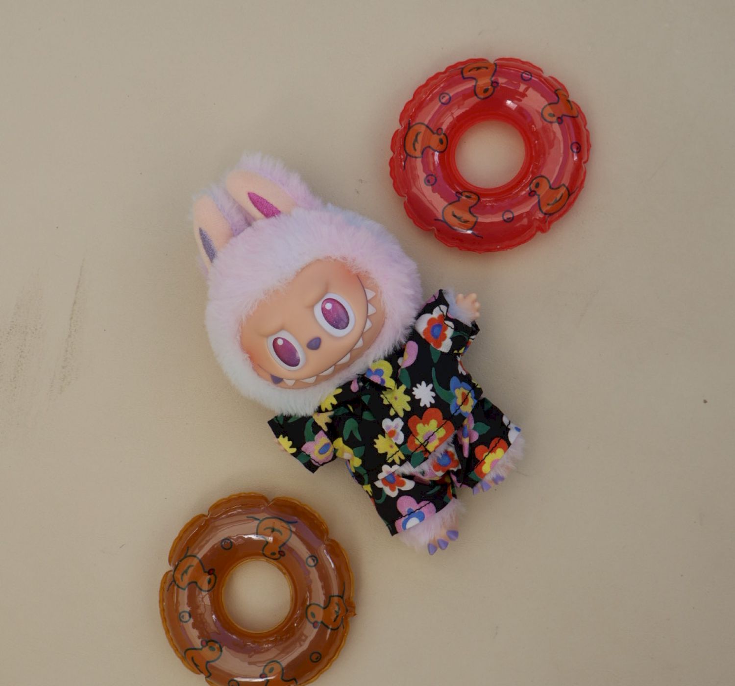 A plush toy dressed in a floral outfit with bunny ears, surrounded by red and brown donut-shaped objects is on display.