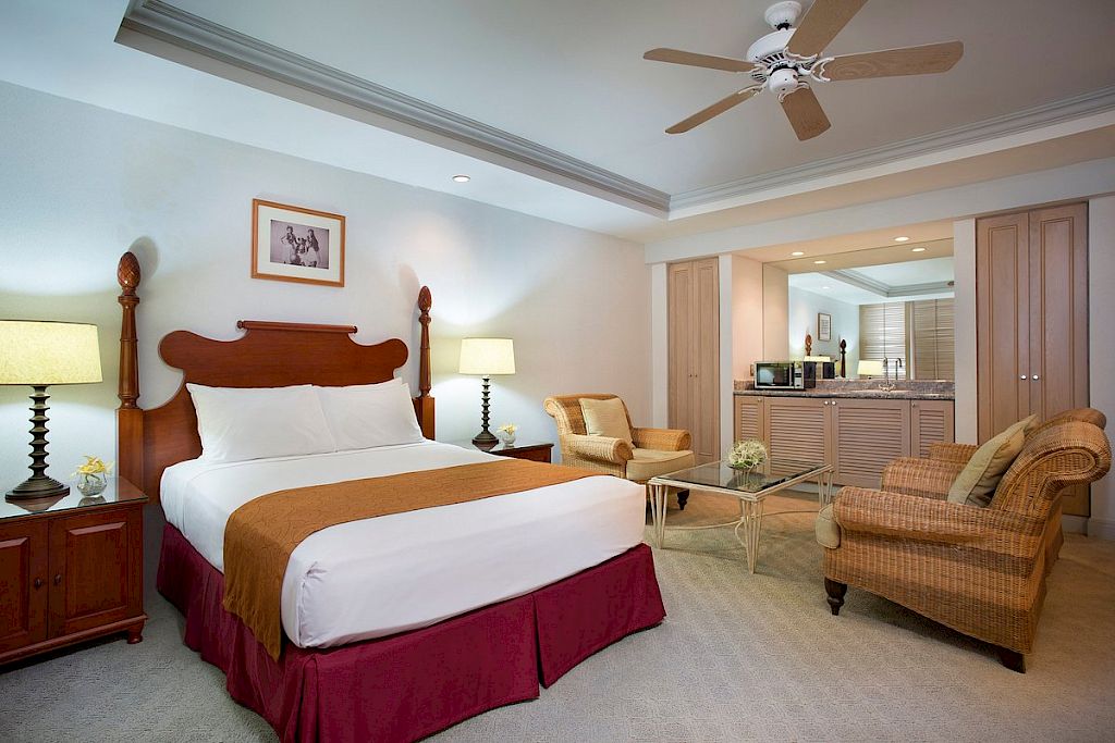 A wide-angle view of a hotel room with a bed, seating area, and kitchenette.
