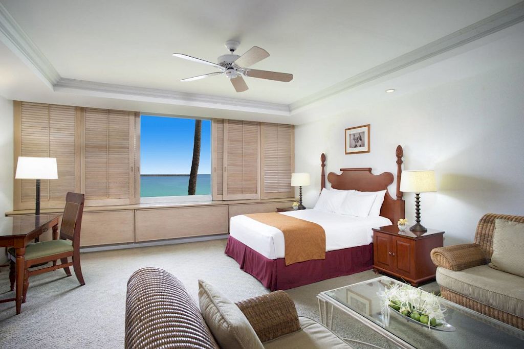 A hotel room with a large bed, sitting area, and ocean view.