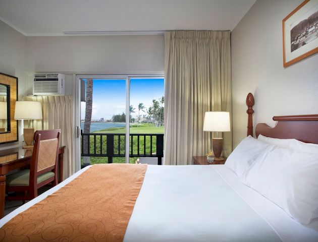 A hotel room with a bed, desk, chair, and window overlooking a balcony with a view.