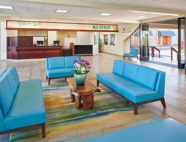 A hotel lobby with blue couches, a wooden coffee table with flowers, and a reception desk in the background.